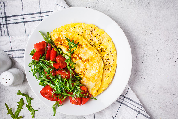 Classic omelet with cheese and tomatoes salad on white plate top view